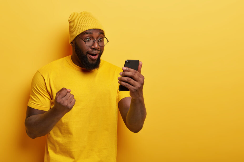 photo-happy-dark-skinned-guy-celebrates-victory-favourite-team-reads-results-game-internet-looks-overjoyed-smartphone-display